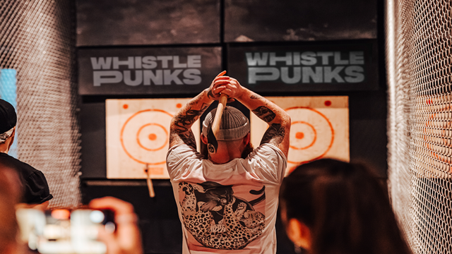 a person taking a photo of another person about to throw an axe into a target board