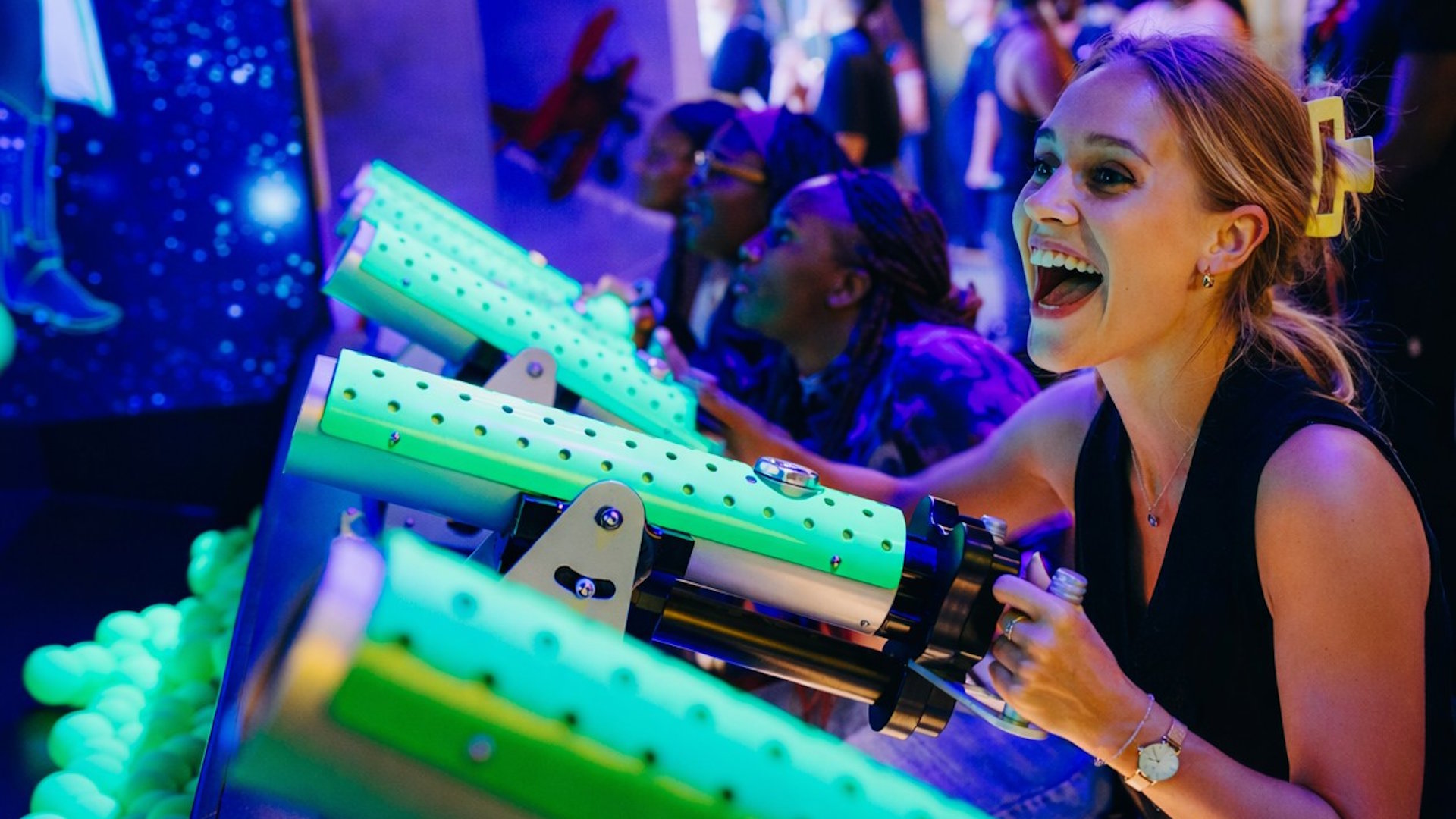 A person smiling as they aim a green toy cannon at a target.