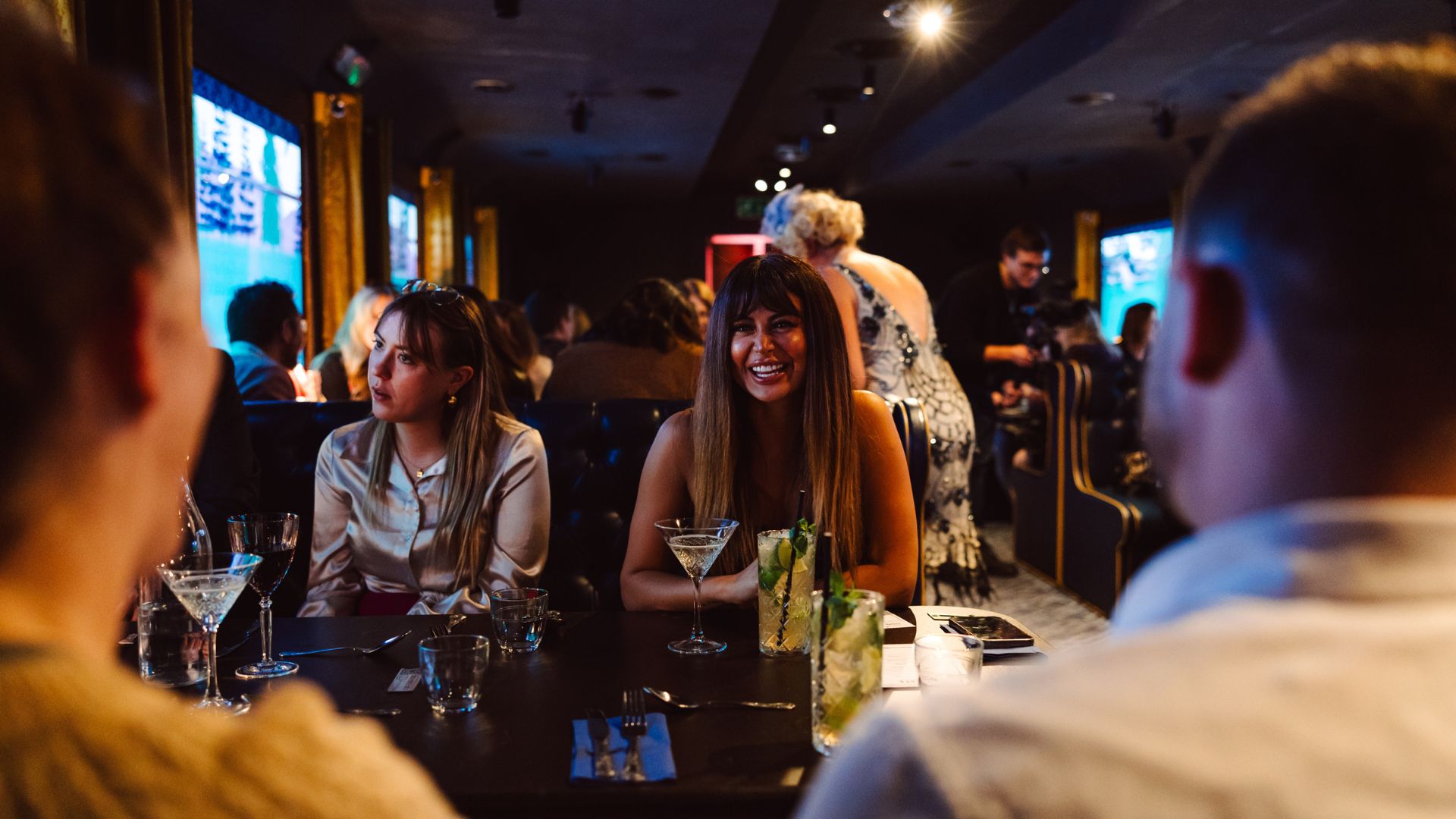 Cocktails, candlelight and a night of immersive storytelling. Image courtesy of Funincular Productions. Group enjoying cocktails and dinner in a dimly lit, lively restaurant setting aboard a murder mystery train experience.