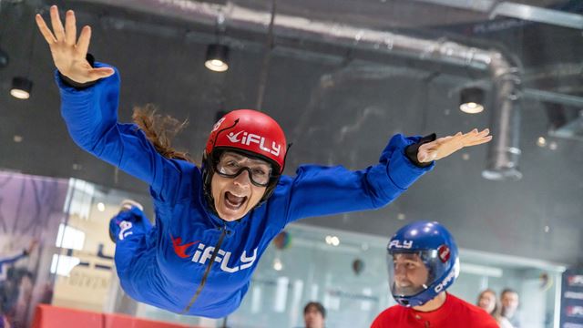 A person experiences indoor skydiving at iFLY at The O2, floating in a vertical wind tunnel while an instructor supervises nearby.