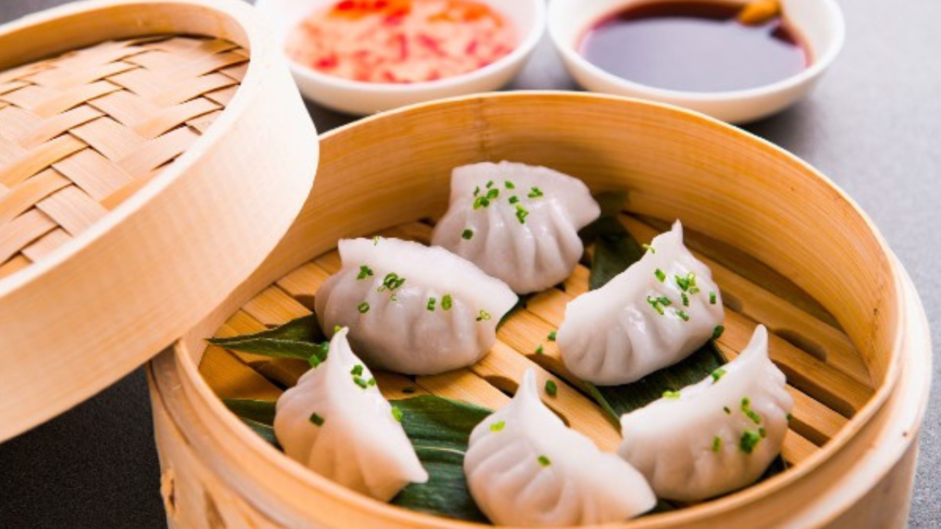 Tuck into delicious dim sum for lunch near Chinatown. Credit: Red Letter Days. Image courtesy of Red Letter Days. Prawn dumplings in a wooden basket with dipping sauces in the background.