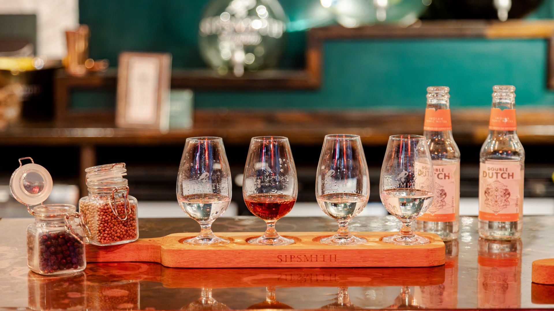 A tasting flight of Sipsmith spirits served in four glasses with botanicals and tonic water on a wooden tasting board.