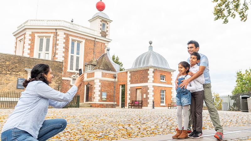 Get ready for a day of family fun at the Royal Observatory in Greenwich. Credit: Royal Observatory Greenwich. Image courtesy of Royal Observatory Greenwich. A mum kneeling to take a photo of her kids and partner in front of the Royal Observatory, Greenwich.