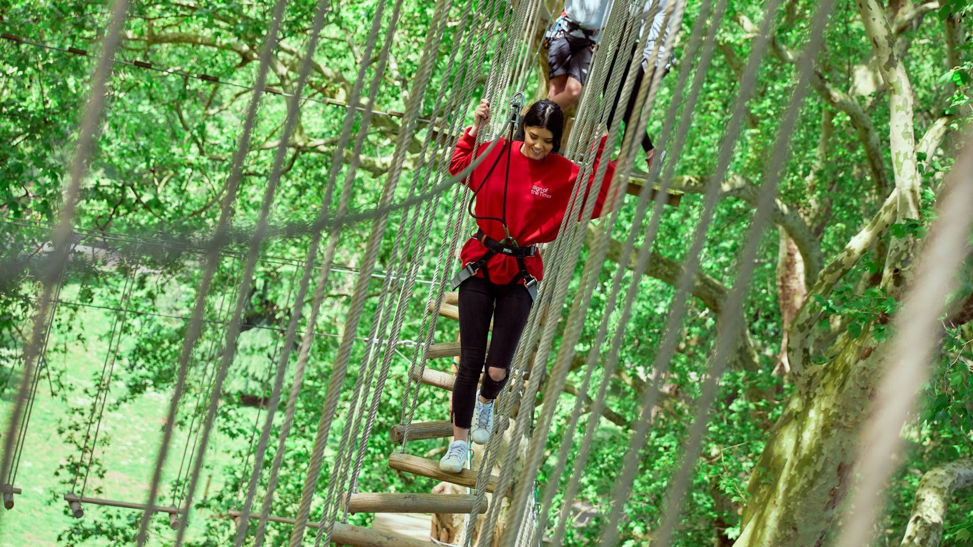 Climb, balance and take on the treetops with an outdoor adventure. Image courtesy of Go Ape. Person navigating a high ropes course among trees, secured with a safety harness.