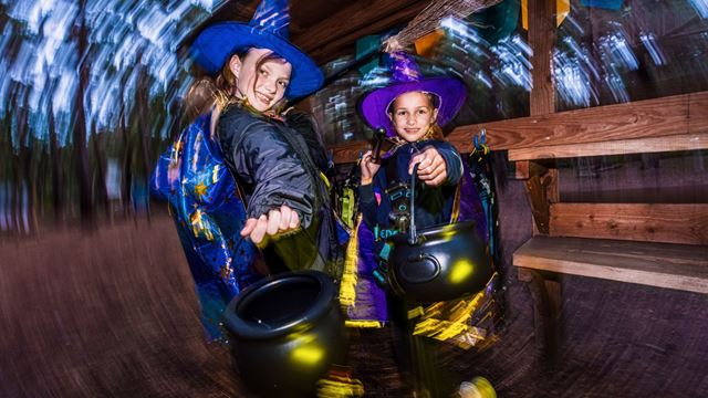 Two young girls wearing witch hats and capes, photographed at a woodland park.