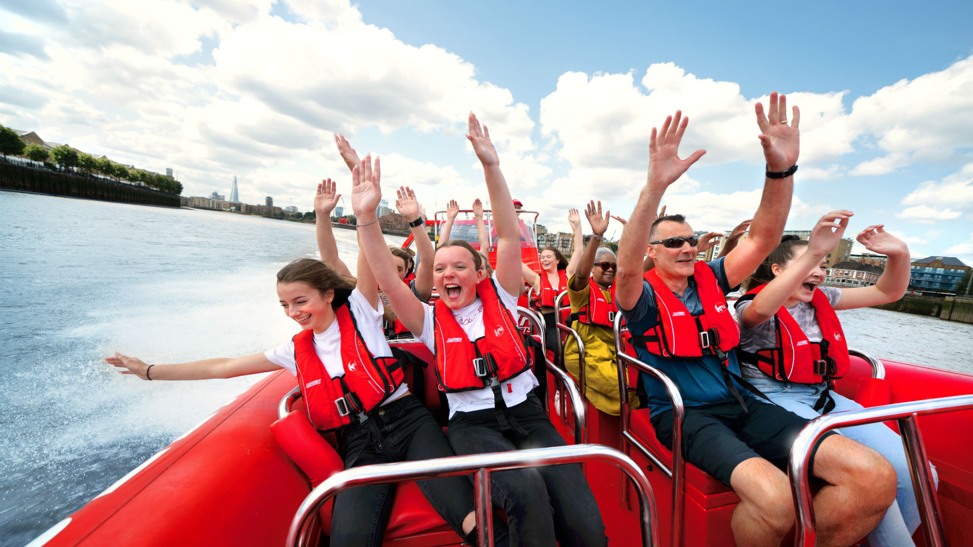 Speed down the Thames while taking in the iconic views of London. Image courtesy of Thames Rockets. People enjoying a boat ride, with their hands up in the air on a bright day.