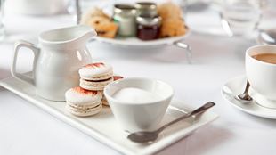 Stack of macaroons next to a cup of tea and tea making ingredients.