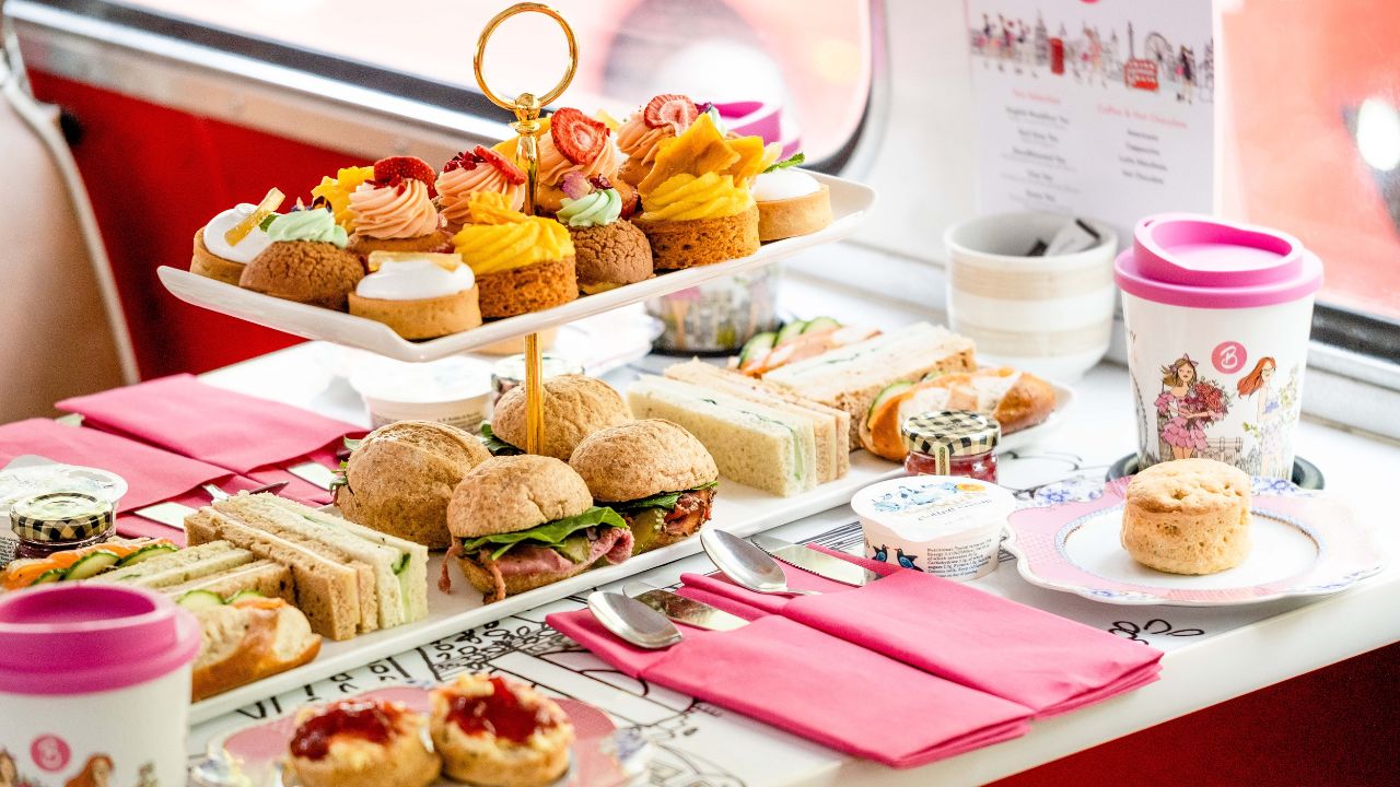A table with afternoon tea standing of savoury and sweet treats, including finger sandwiches, cakes and pastries.