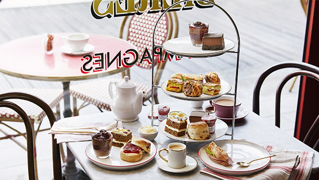 A white table with cups and afternoon tea cakes and finger sandwiches.