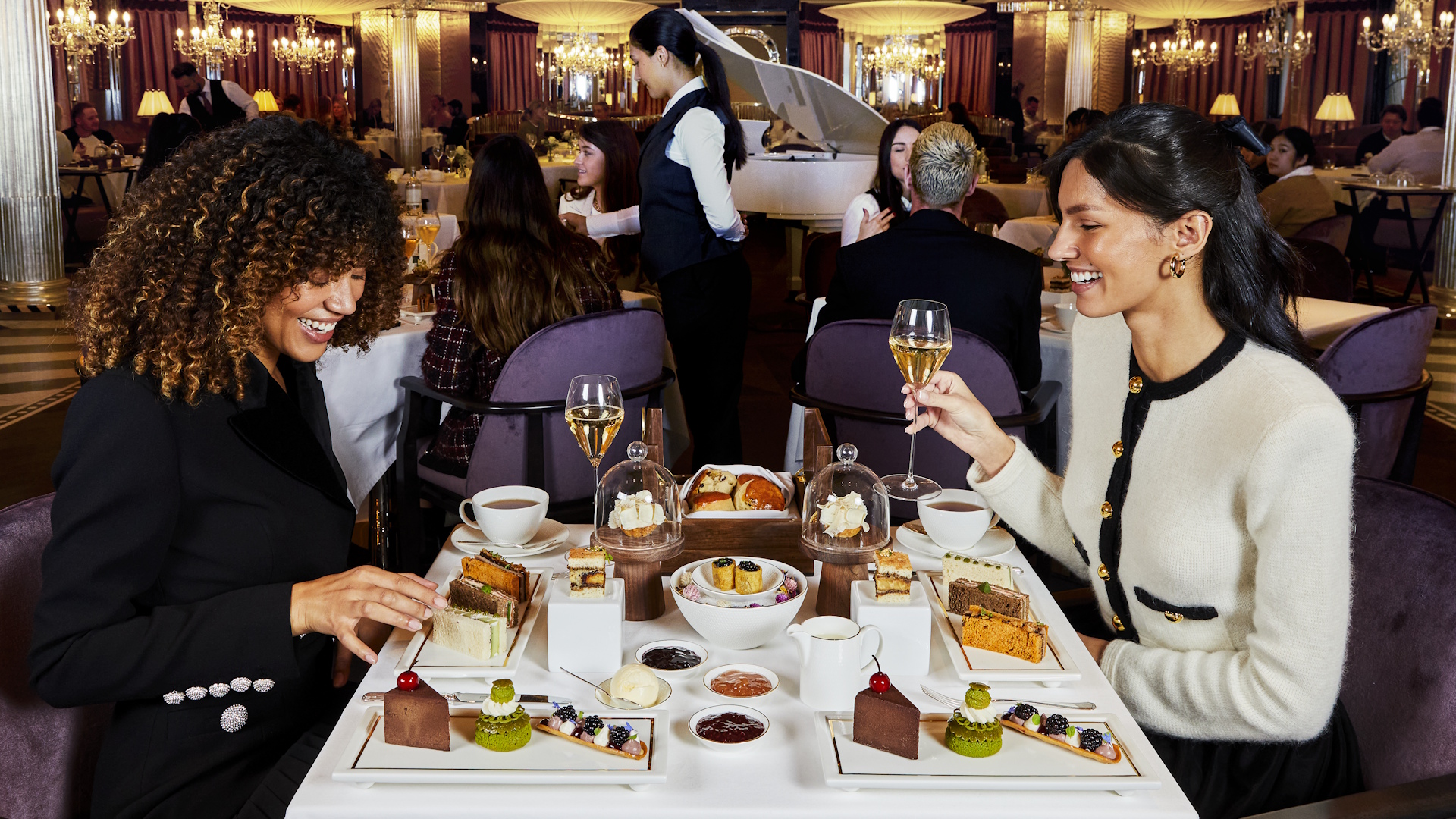 Enjoy a champagne afternoon tea at The Georgian. Image courtesy of Harrods. Two women smile as they tuck into champagne afternoon tea treats inside Harrods' 1920s-style Georgian salon.