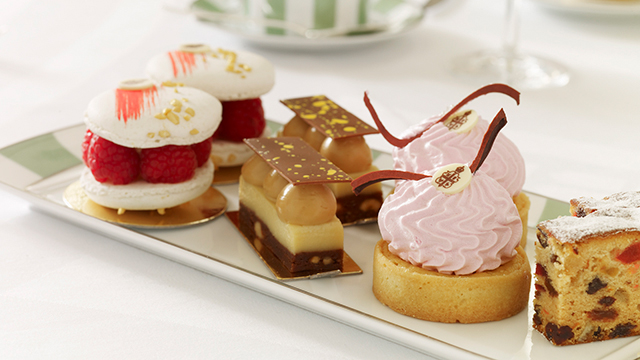 Claridge's afternoon tea. Image courtesy of Maybourne Hotel Group. Seven small, colourful cakes on a green-and-white-striped plate.