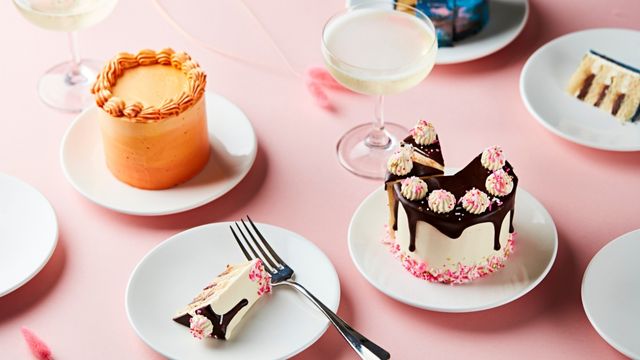A pink table with white plates and brightly iced cakes.