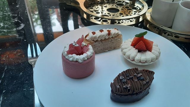 A plate with four little sweet desserts including a small chocolate cake and a strawberry and cream tartlet.