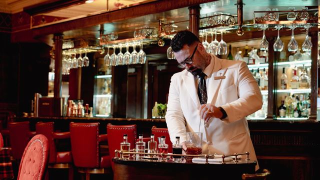 Bartender in a white jacket preparing a Negroni from a trolley in the New York Bar at The Rubens.