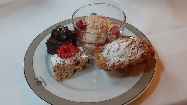 A plate with a chocolate cake, a carrot cake, some deconstructed crumble with cream and a flapjack.