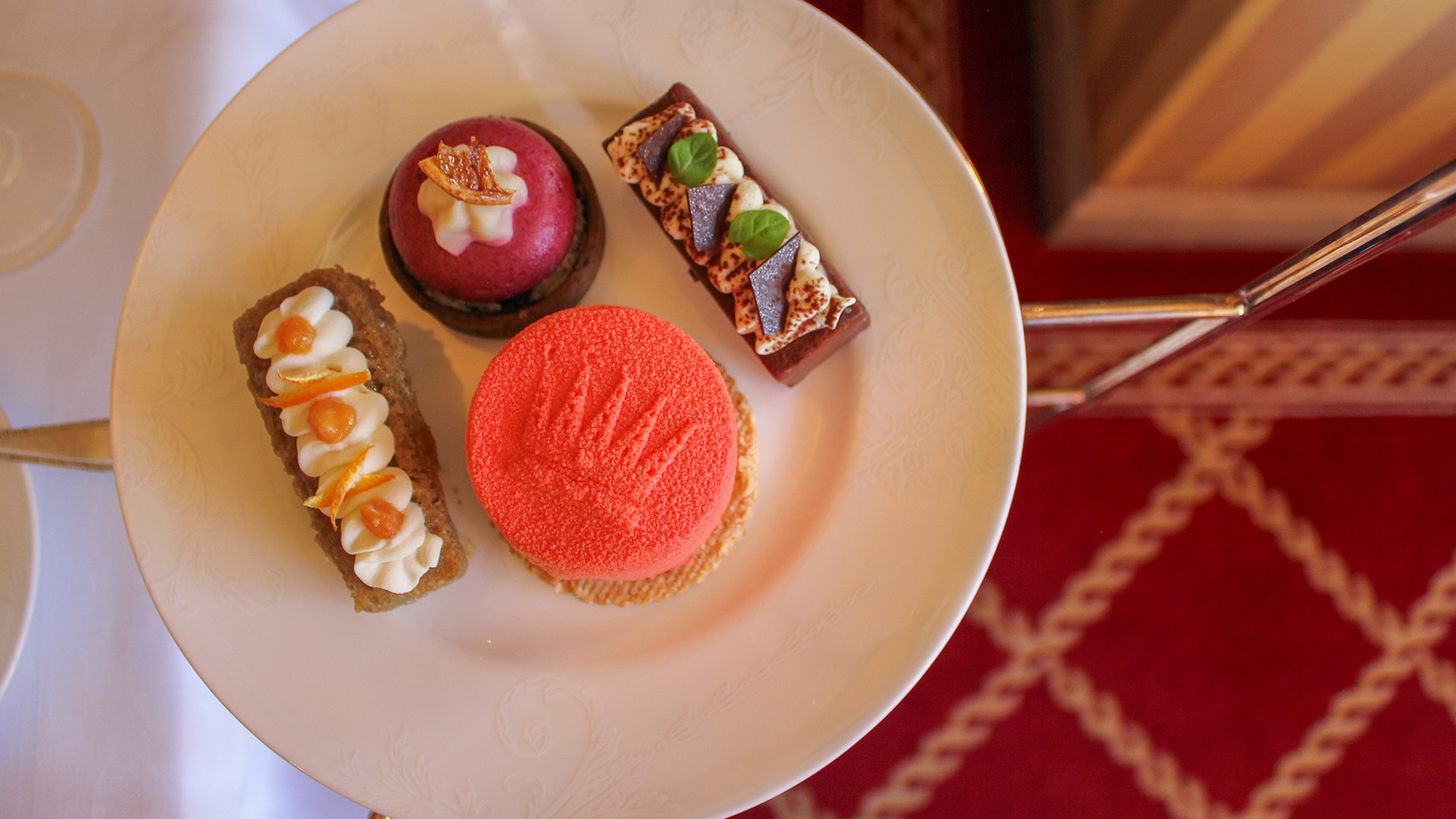 Enjoy a vegan afternoon tea in an elegant setting at The Rubens at the Palace. A set of four small dessert cakes on a white plate with vibrant colours.