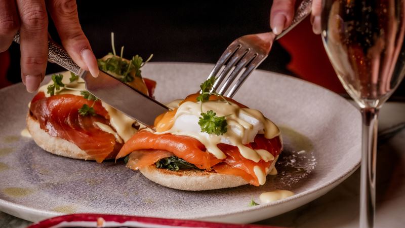 Tuck in to brunch made the Italian way at Bocconcino restaurants across London. Credit: Bocconcino. Image courtesy of Bocconcino. A photo of a woman's hands cutting into a poached egg on an Italian-inspired salmon and eggs benedict