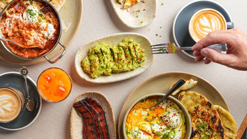 Tuck into a selection of mouthwatering brunch plates at Caravan. Credit: Caravan. Image courtesy of Caravan. A bird's-eye photo of plates of food on a table at Caravan with brunch items including smashed avocado, shakshuka and bacon