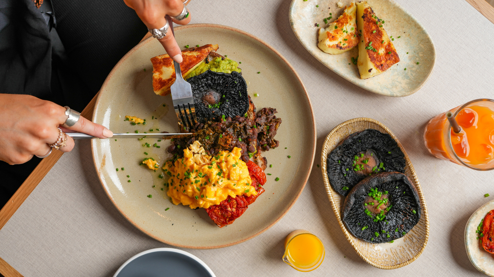 A bird's-eye photo of a table at Caravan filled with brunch items including scrambled eggs, mushrooms, tomatoes, avocado and halloumi