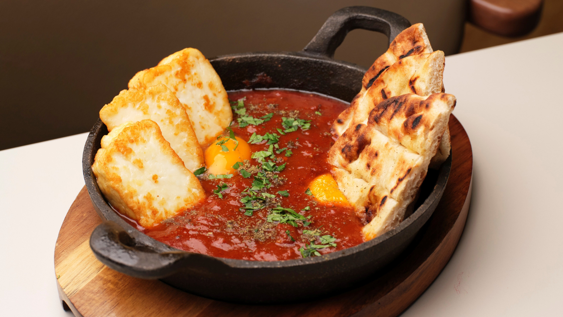 A phot of a portion of shakshuka from CERU with halloumi, eggs and flatbread in a rich tomato sauce garnished with parsley