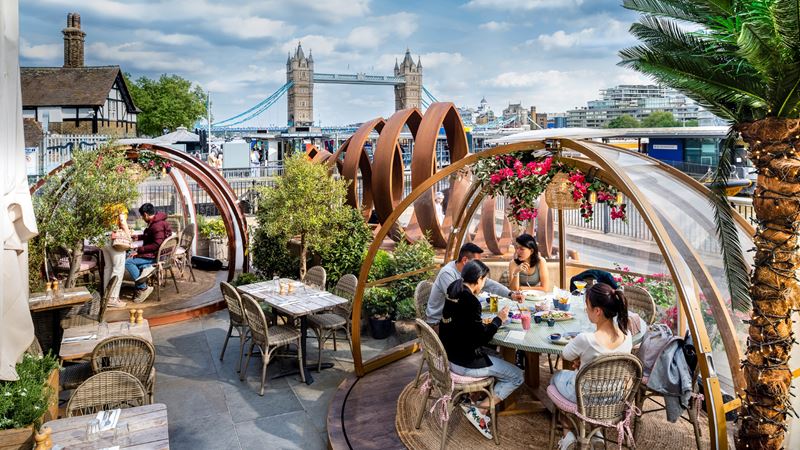 Tuck into a delicious brunch with a view of Tower Bridge from your very own covered igloo. Credit: Allan Stone. Image courtesy of Coppa Club. A photograph of two covered igloos in the Coppa Club garden with people sat on chairs inside them eating and drinking with a view of Tower Bridge in the background