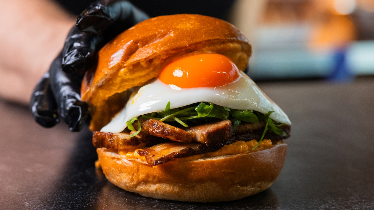 A photo of a brioche breakfast roll from Eggslut with a bright orange sunny side up fried egg on top of rocket and meat
