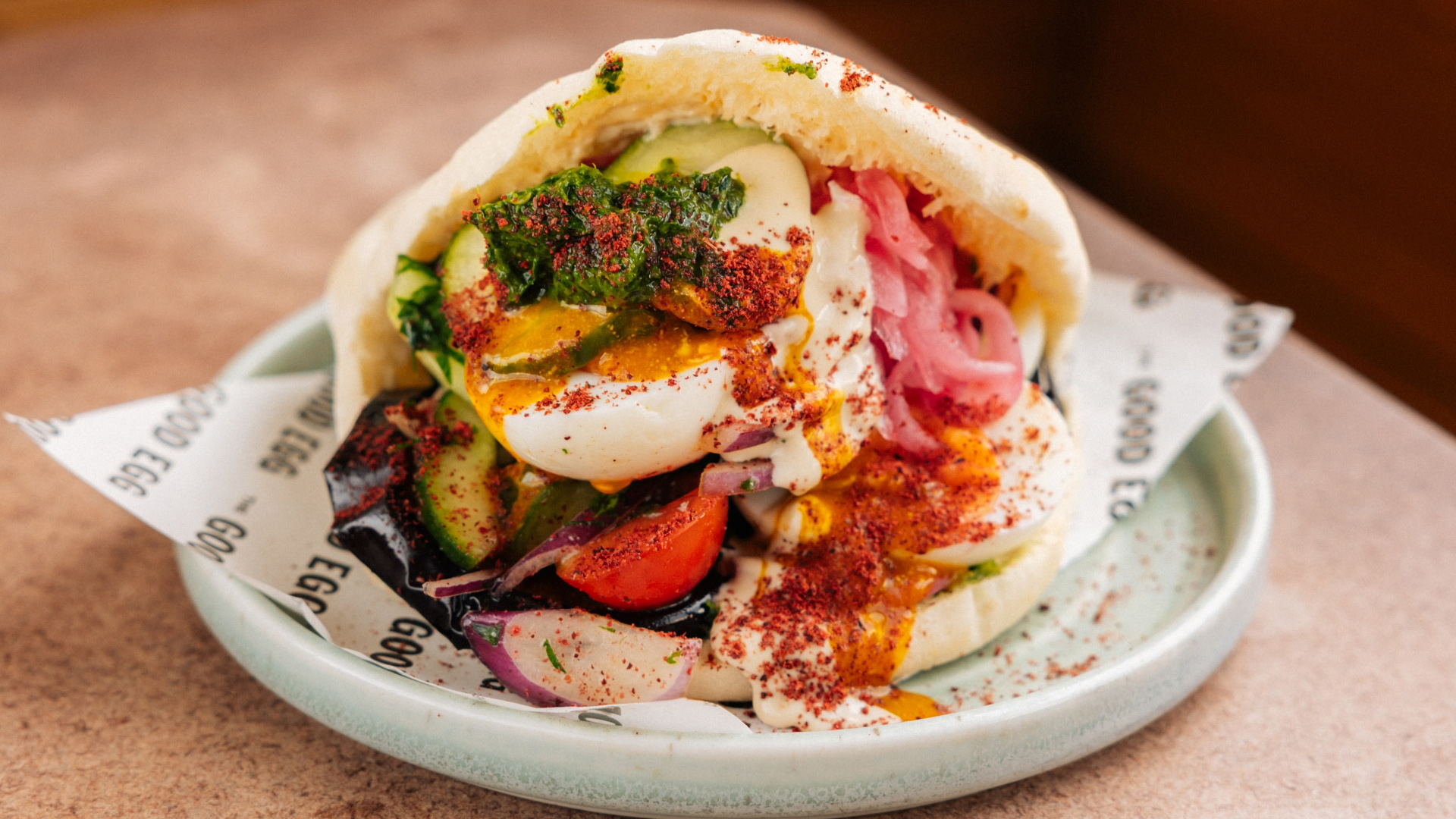 A photo of a breakfast pitta at The Good Egg filled with egg, pickled red onions, herbs and sauces