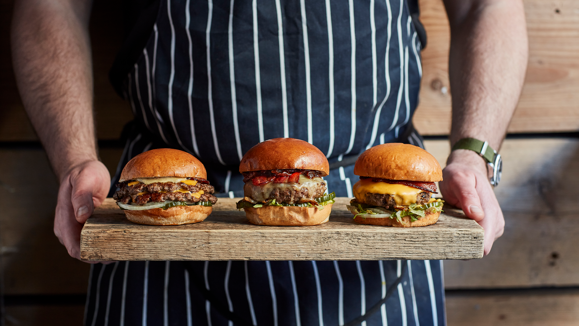 A trio of burgers on a tray held by a chef