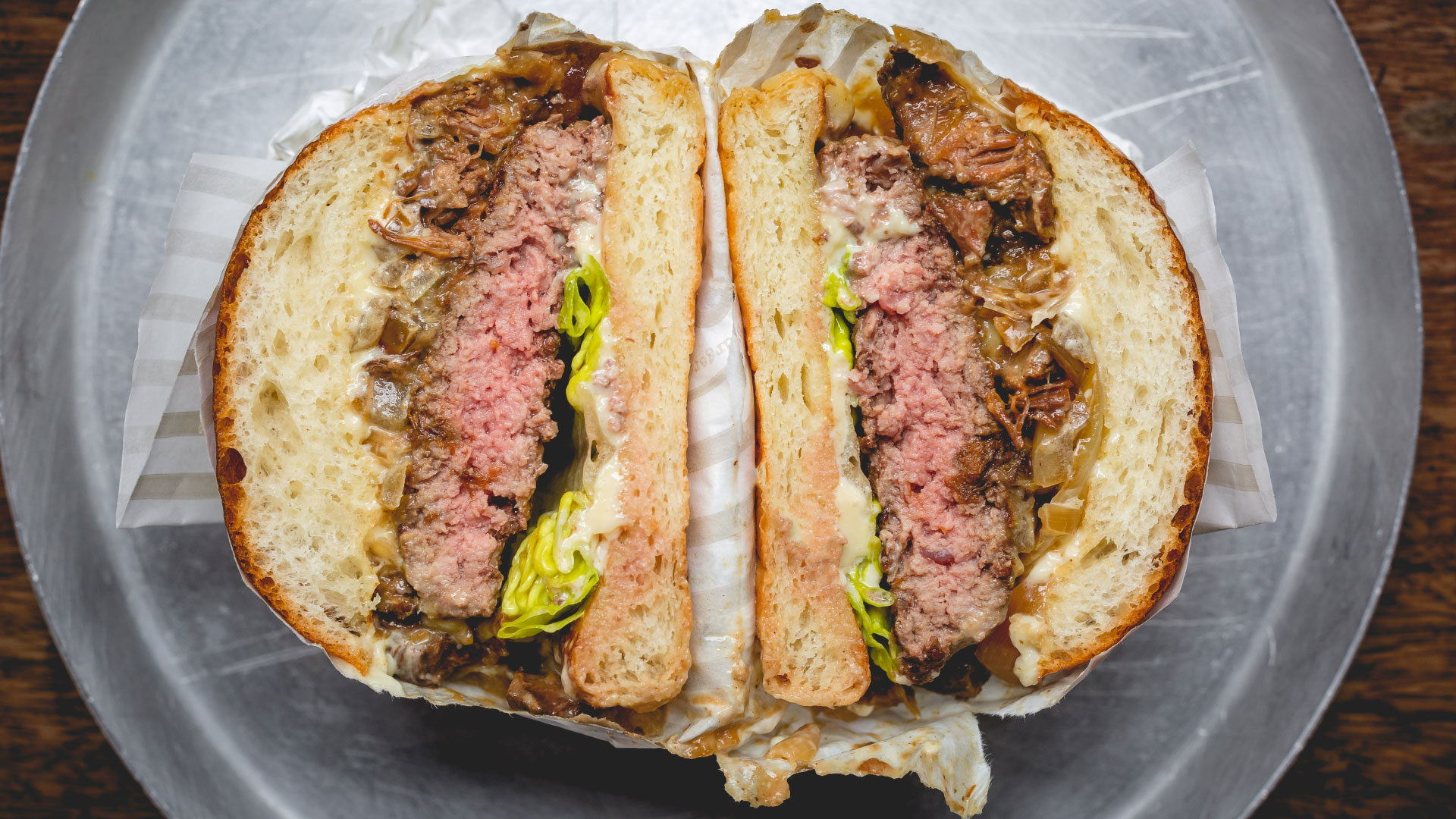 A bird's-eye photo of a Patty & Bun burger sliced in half, showing the thick beef patty pink in the middle with caramelised onions, lettuce and a mayo based sauce