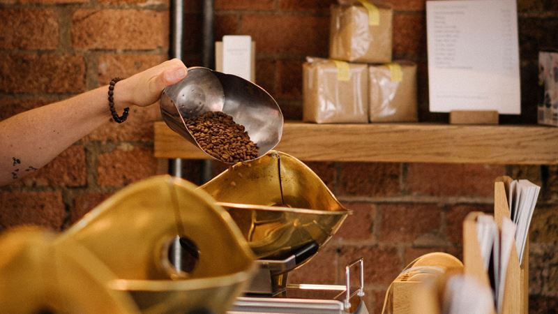 Find unique and secret cafes and bars across the capital. Image courtesy of Monmouth Coffee Company. A close up photo of a hand holding a big metal scoop filled with coffee beans being poured into gold weighing scales inside Monmouth Borough