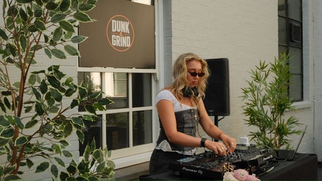 DJ performing at a Dunk & Grind event at Mercato Metropolitano, with plants and speakers surrounding the DJ booth.