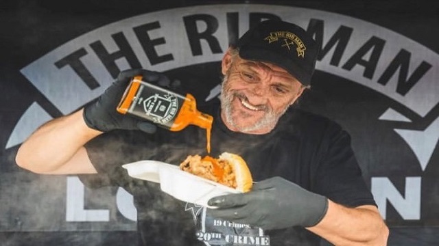 A man pouring a bottle of hot sauce onto the baby rib roll he is holding