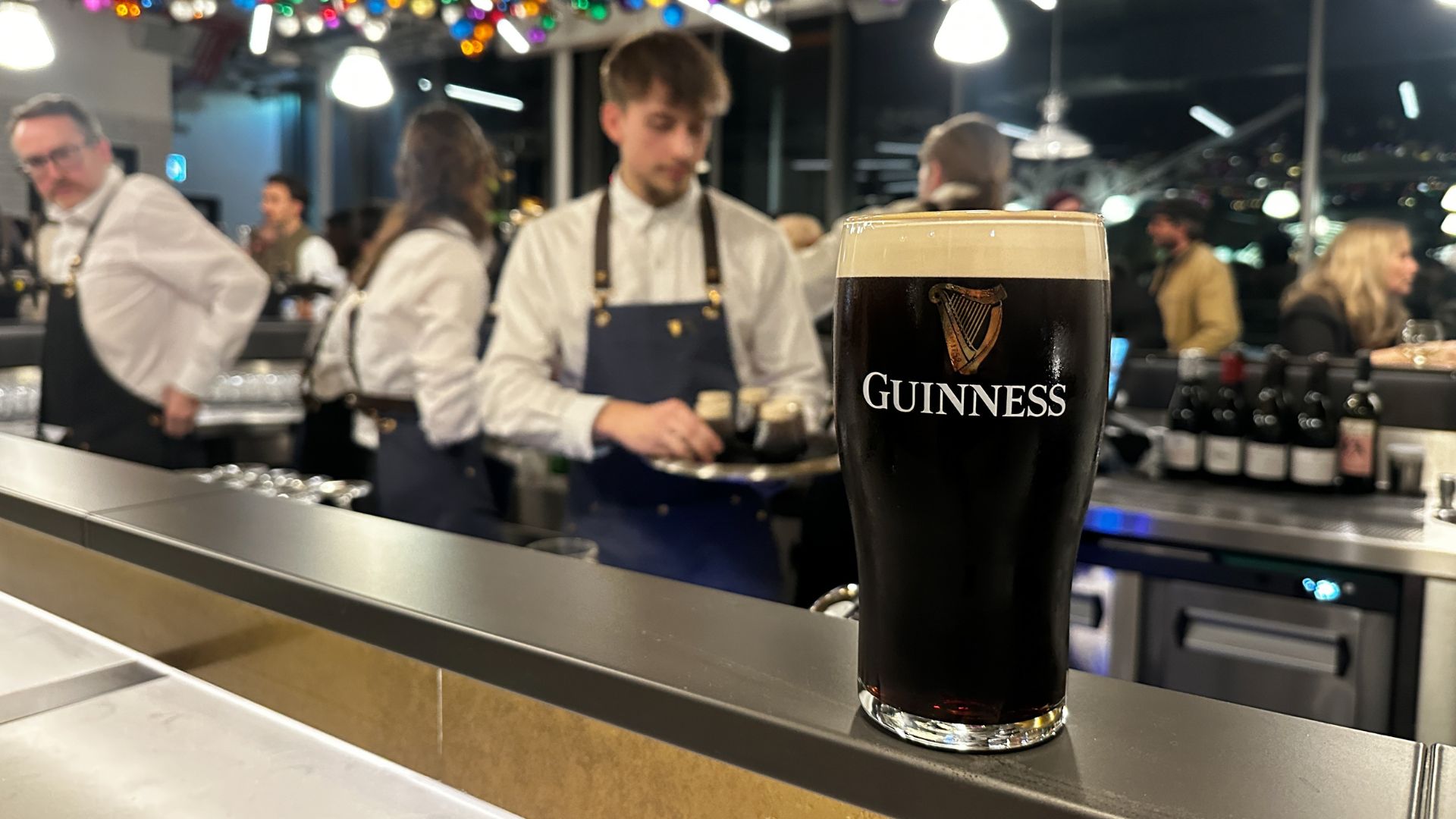 A classic pairing: fresh oysters and a pint of Guinness at the brewery’s Oyster Bar. Image courtesy of Kirstine Spicer. A pint of Guinness sitting on a bar counter at the Guinness Open Gate Brewery Oyster Bar, with chefs working in the background.