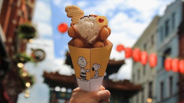 A hand holds a waffle cone filled with vanilla ice cream in Chinatown, London.