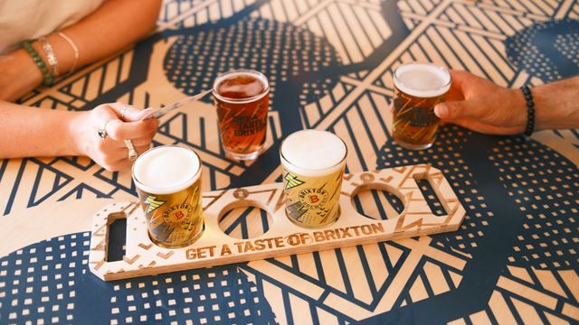 A flight of beers during a taproom tasting with two people next to them at Brixton Brewery.