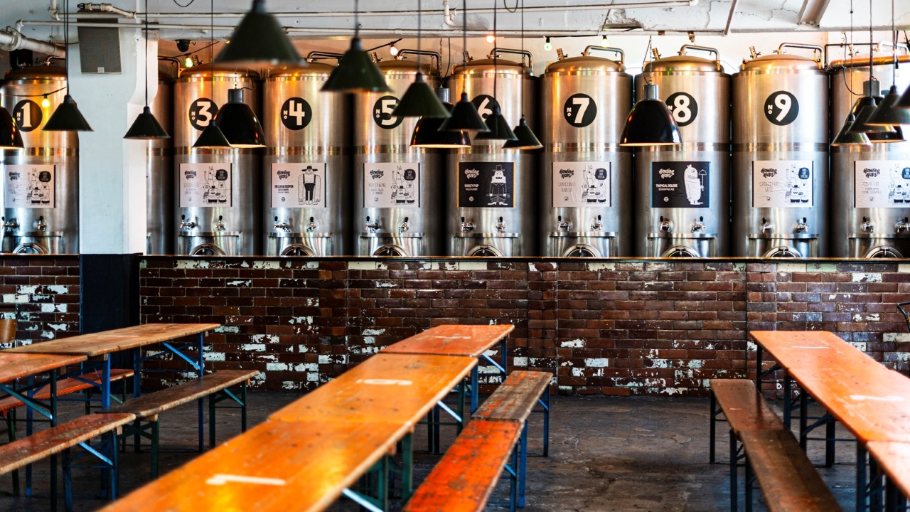 A photo of the brewing tanks lining the industrial Howling Hops brewery in Hackney with low hung lamps and bench seating