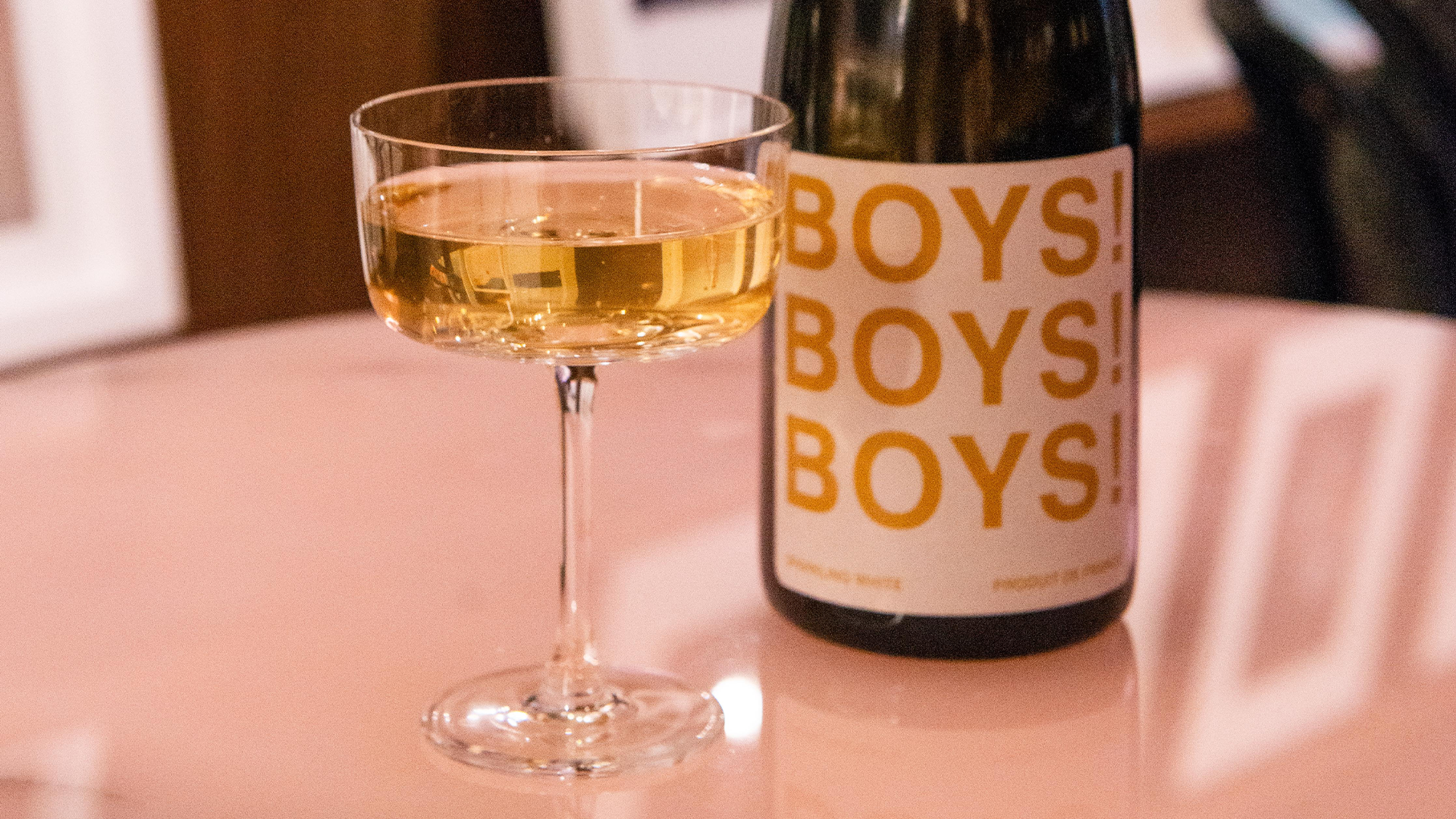 A glass of white wine alongside a BOYS! BOYS! BOYS! branded bottle of wine