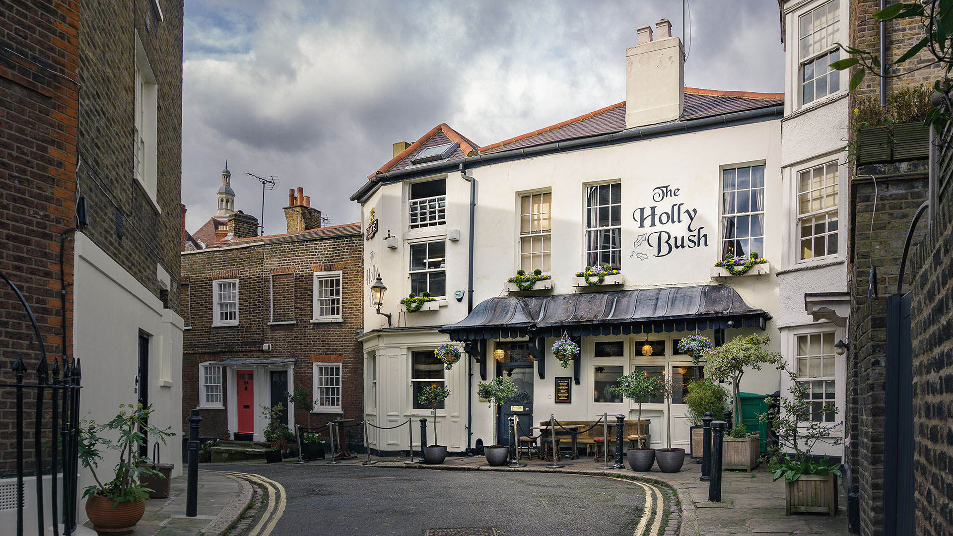 The facade of The Holly Bush pub in Hampstead and the street leading up to it on a clear day.