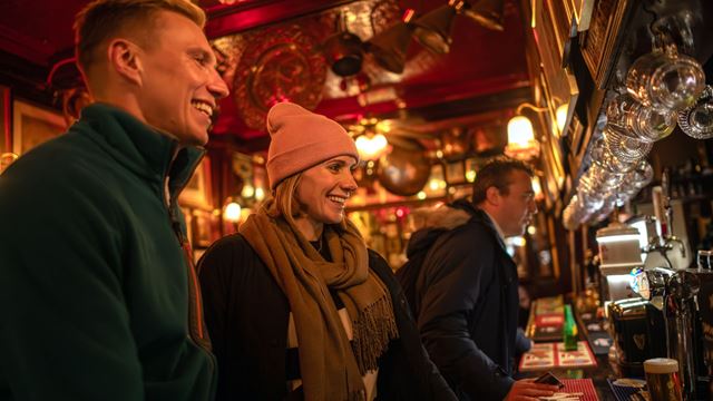 Man and woman smiling as they stand at the bar at a traditional London pub