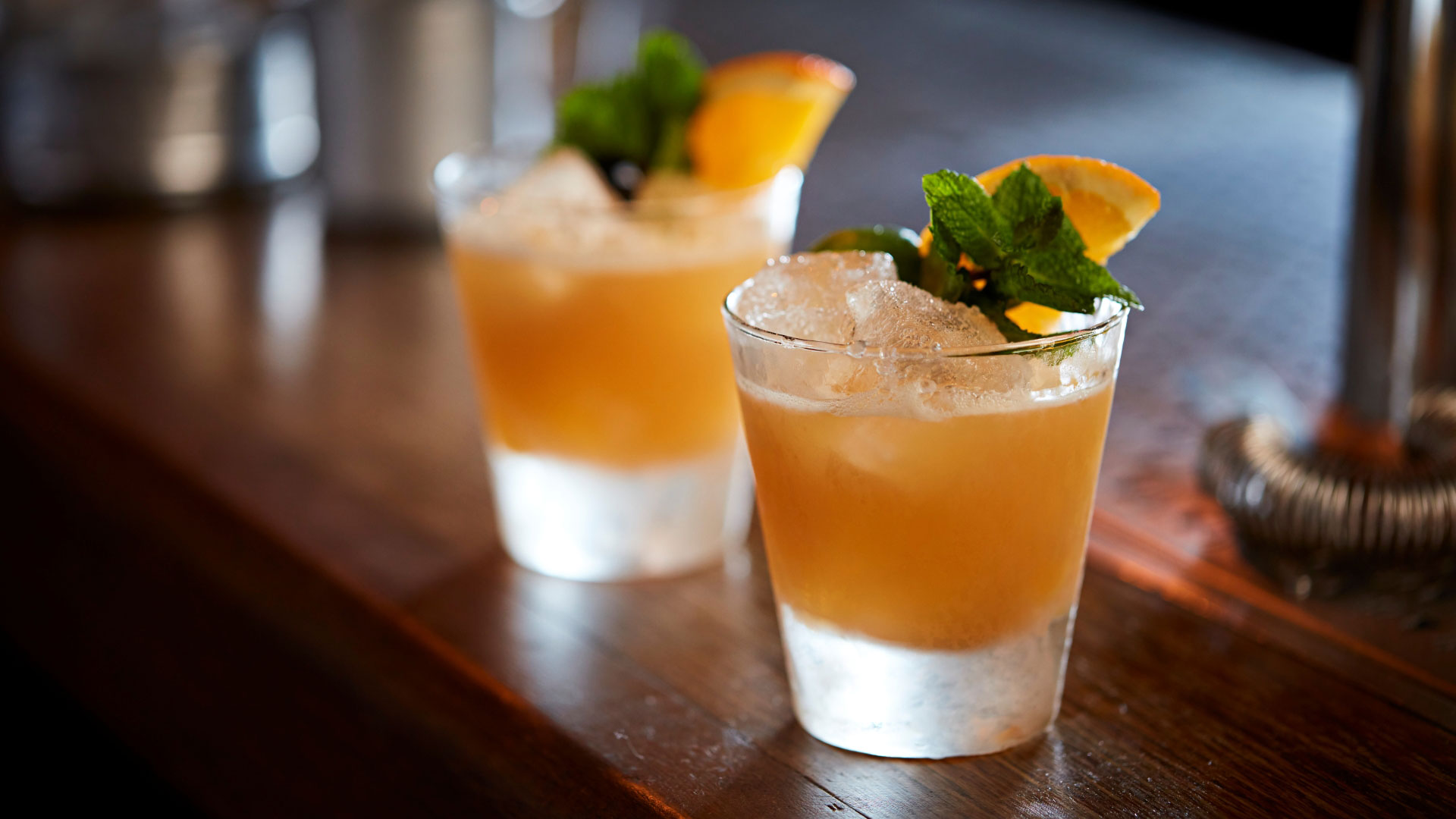 A photo of two frozen orange cocktails in short glasses garnished with a slice of orange and mint leaves at Satan's Whiskers cocktail bar