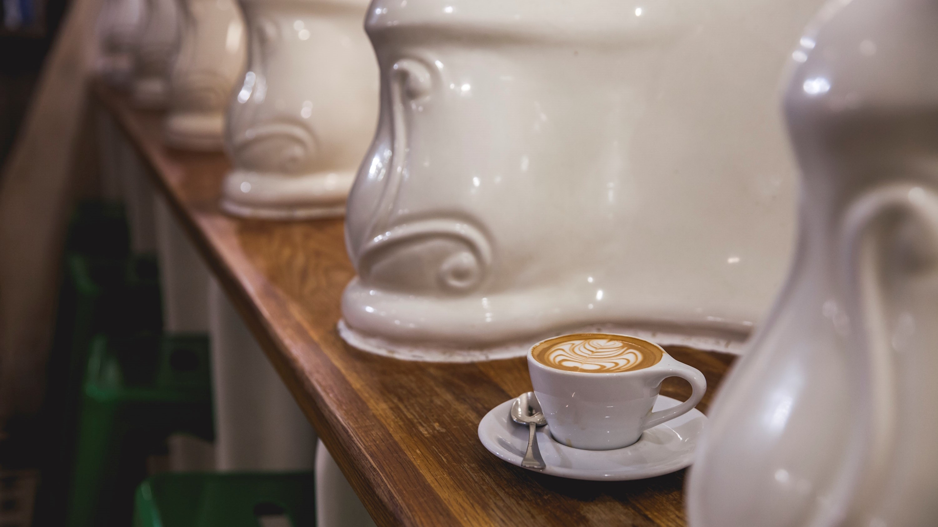 Cup of coffee on wooden counter surrounded by old Victorian urinals repurposed as decoration in quirky London cafe.