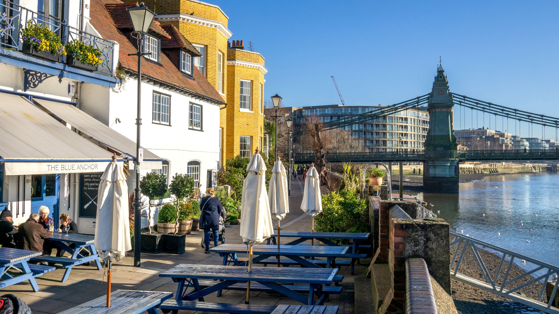 A photo of the exterior of The Blue Anchor on the river Thames on a bright sunny day with blue picnic benches outside the front