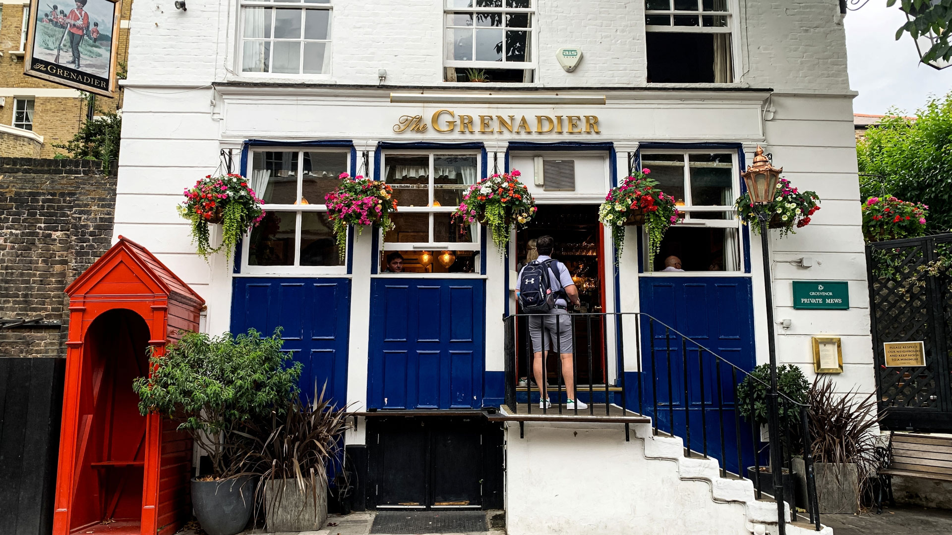 A photo of the exterior of The Grenadier in Belgravia, a standalone white Victorian building with stairs leading up to the front door and flower baskets handing outside