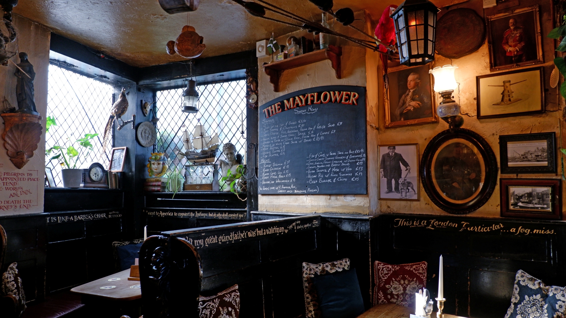 Interior of the warm lit Mayflower pub in London with traditional features covering the walls including framed pictures and a blackboard with a wooden table and chairs in the foreground