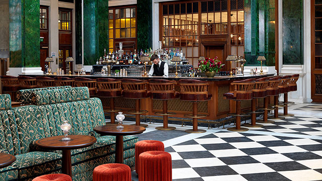 The Nickel Bar at The Ned © The Ned. Image courtesy of The Ned The American-style Nickel Bar at The Ned with elegant green sofas and interior and a bartender serving drinks