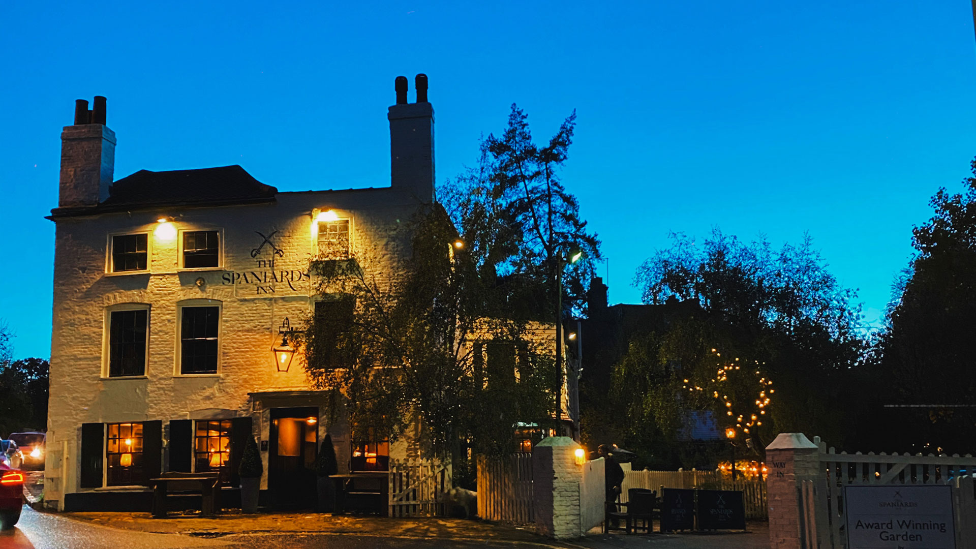 The facade of The Spaniards Inn pub in Hampstead lit up at night with clear dark blue skies.