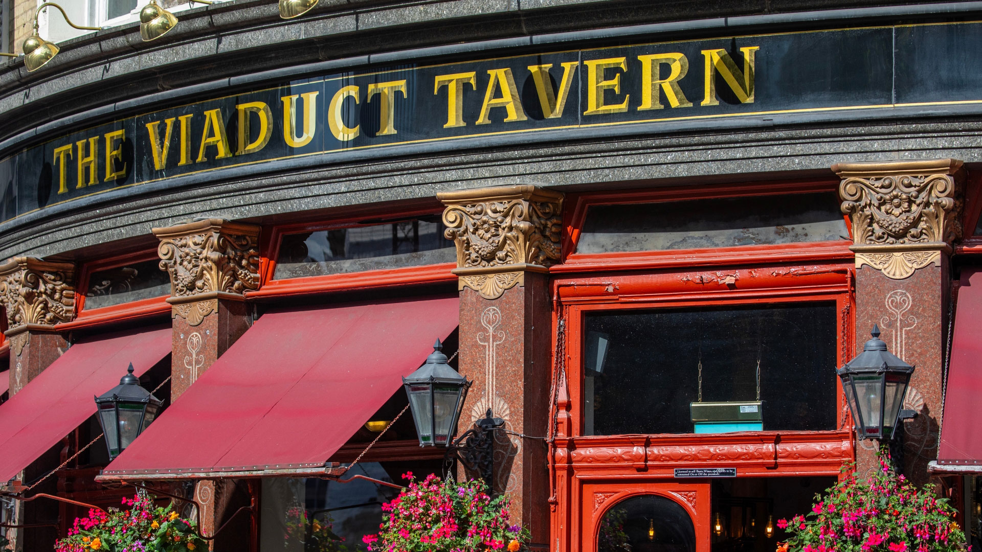 A close up photo of the exterior of The Viaduct Tavern with gold lettering on a black background and red painted door