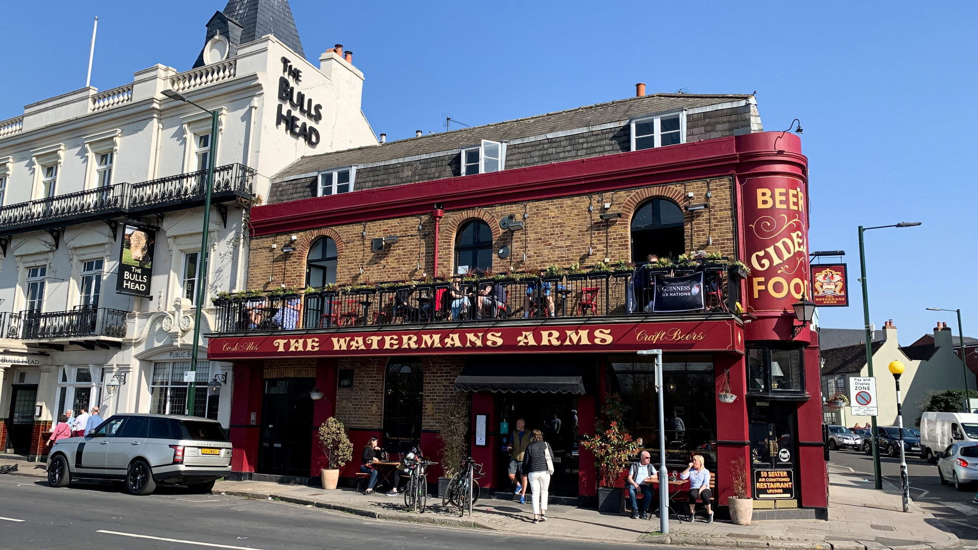 A photo of the Waterman's Arms pubs from the front on a bright sunny day with people stood and sat on benches outside