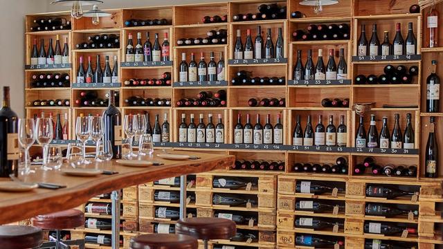 Brown shells lines with many bottles of wine next to a table with wine glasses.