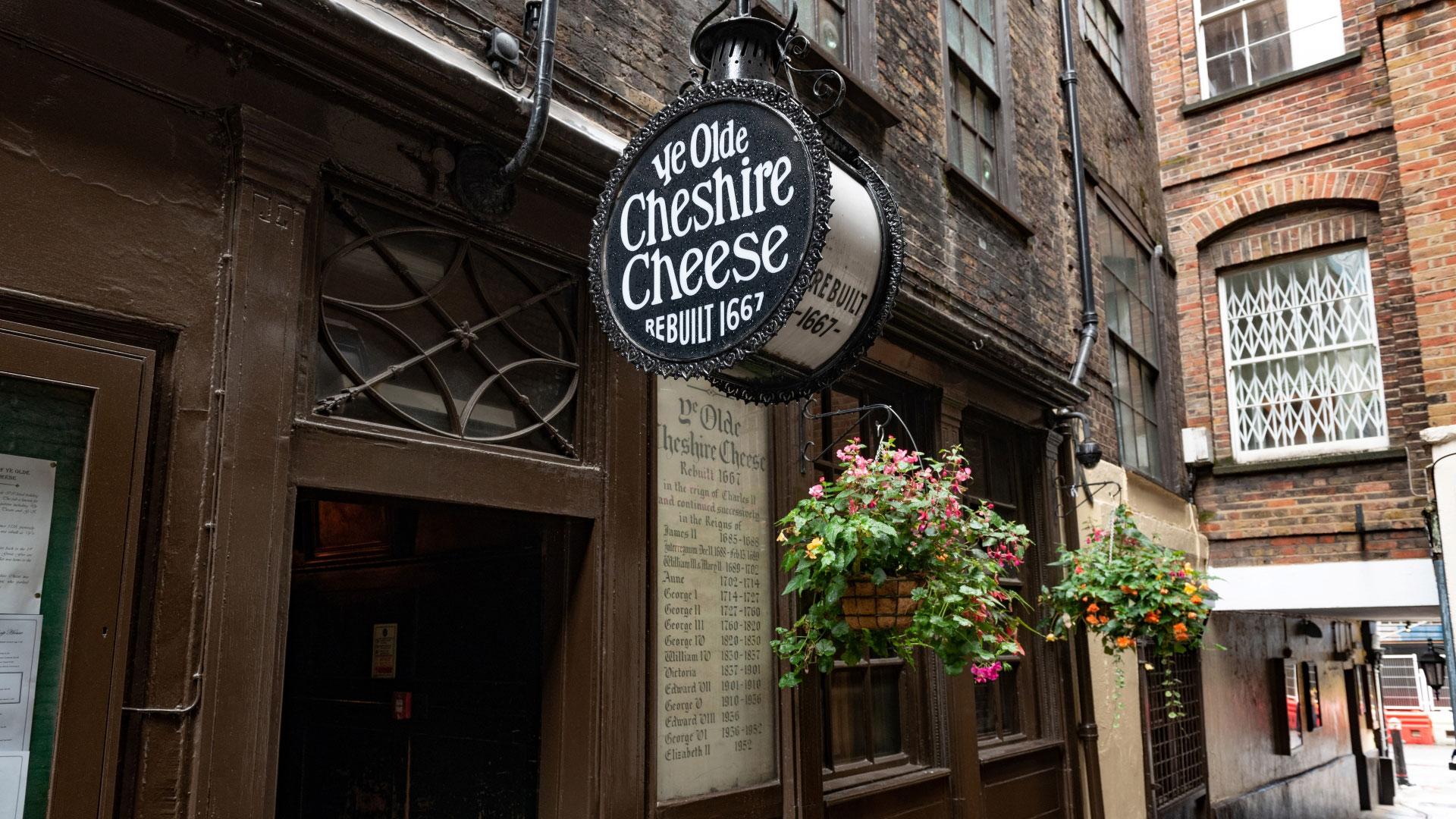 A photo of the exterior of Ye Olde Cheshire Cheese with the round sign outside and hanging baskets with flowers in the windows
